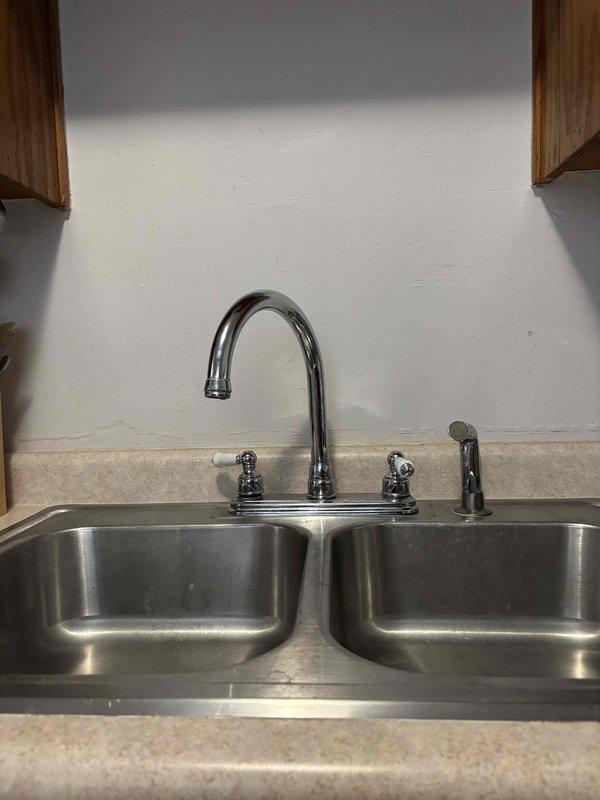 Successfully completed kitchen faucet replacement as requested by customer. Installed new customer-supplied faucet with dual control knobs and separate sprayer attachment onto double-basin stainless steel sink. Tested water flow and confirmed proper operation with no leaks.