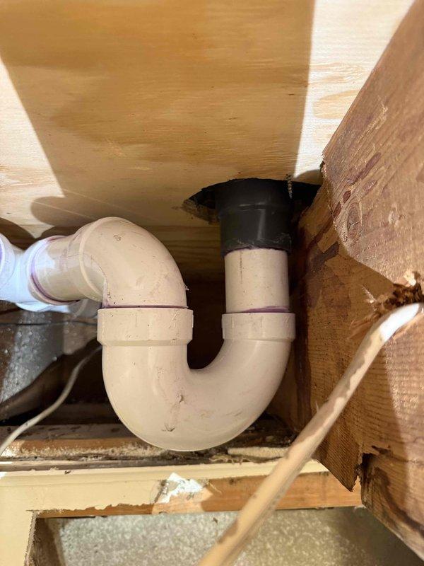 Completed repiping of shower drain system, installing new PVC P-trap assembly with proper drainage connections. Replaced deteriorated components with code-compliant piping, securing all connections with appropriate clamps and fasteners to wooden structural supports. Installation included proper elbow joints and horizontal drain runs to ensure optimal water flow and prevent future leakage.