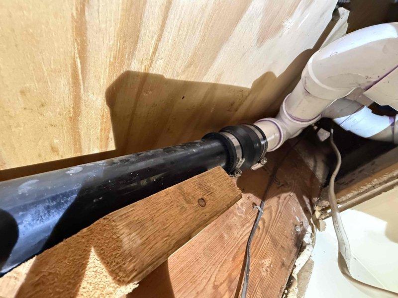 Completed repiping of shower drain system, installing new PVC P-trap assembly with proper drainage connections. Replaced deteriorated components with code-compliant piping, securing all connections with appropriate clamps and fasteners to wooden structural supports. Installation included proper elbow joints and horizontal drain runs to ensure optimal water flow and prevent future leakage.