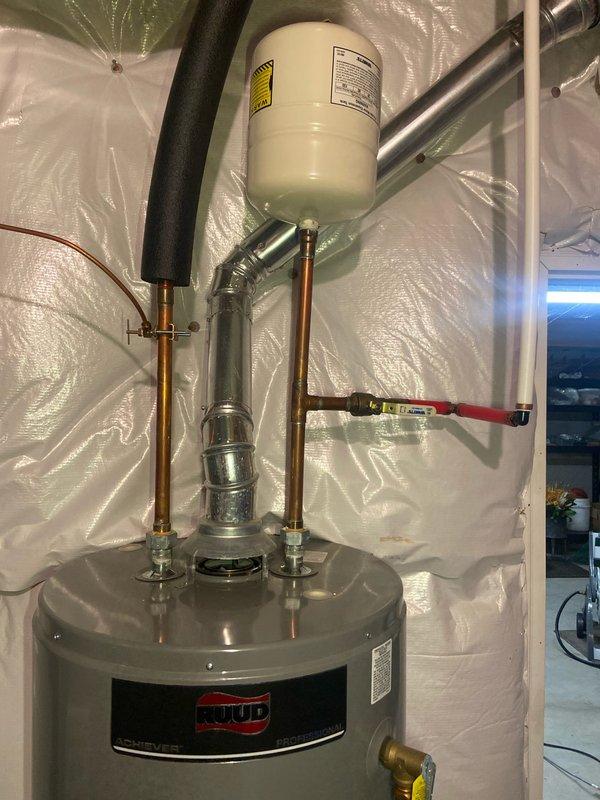 Completed inspection of existing water heater system in basement for replacement estimate. System includes a RUUD tank water heater with copper piping, expansion tank, and red-handled valve. Pressure gauge testing showed reading of approximately 80-90 PSI, which is at the upper acceptable limit for residential plumbing systems.