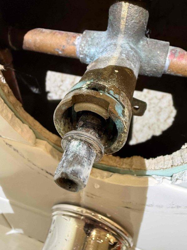 Repaired bathroom tub assembly by replacing corroded T-junction valve and pipe fittings that were causing water leakage around the faucet handle. Accessed plumbing through ceiling/wall cutout, removed mineral-encrusted components, and cleared slow drain blockage to restore proper water flow and drainage functionality.