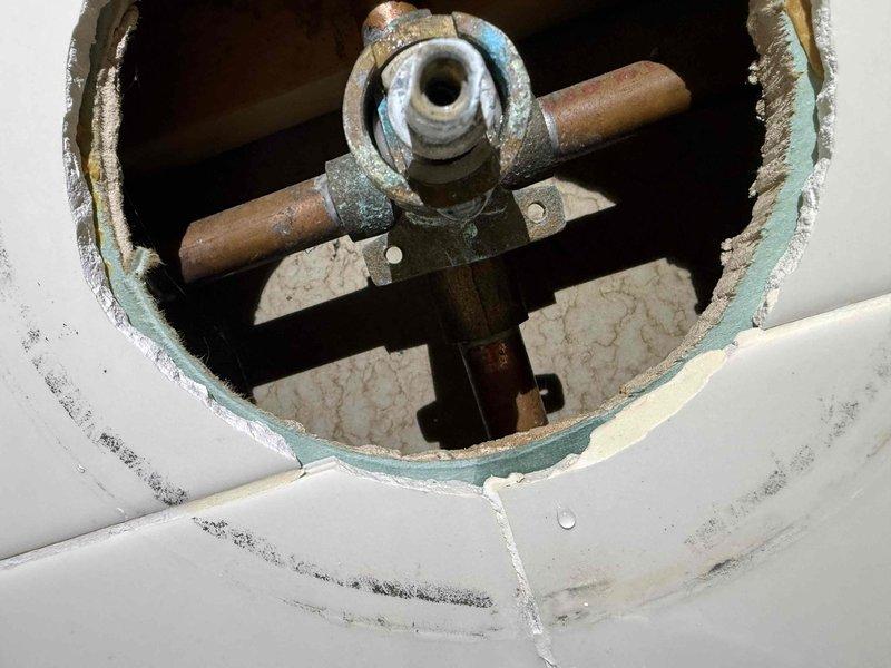 Repaired bathroom tub assembly by replacing corroded T-junction valve and pipe fittings that were causing water leakage around the faucet handle. Accessed plumbing through ceiling/wall cutout, removed mineral-encrusted components, and cleared slow drain blockage to restore proper water flow and drainage functionality.