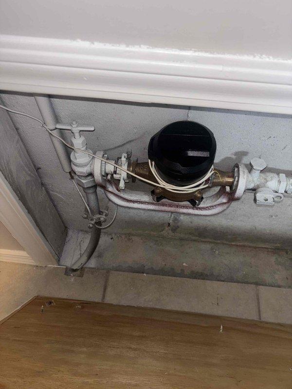 Performed inspection of water heater system, checking flue connection and washer valve as requested. Documented existing installation which includes copper supply lines with appropriate hot/cold connections, metal ventilation elbow, and proper wall insulation. Also inspected water meter assembly with brass fittings and PVC connections. Reviewed preventative maintenance agreement options with customer.