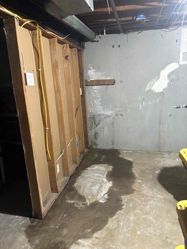 Conducted site assessment for sump pump installation with battery backup in basement showing signs of water infiltration, as evidenced by moisture staining on concrete floor and wall damage. Evaluated existing drainage conditions and exterior discharge options, noting the need for proper connection to the existing exterior drainage pipe system along the foundation.