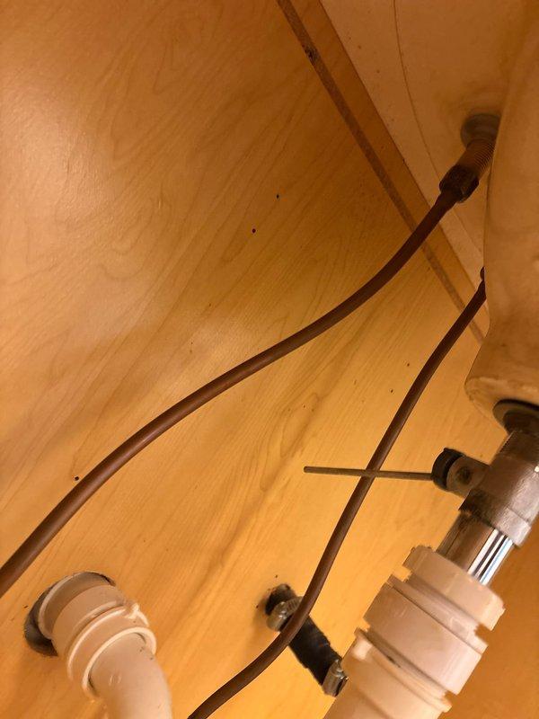 Diagnosed and repaired bathroom faucet leaking into cabinet below. Inspected the plumbing connections inside the wooden cabinet housing the PVC pipe fittings and resolved the leak. Verified proper operation of the chrome dual-handle faucet with no further leakage present.