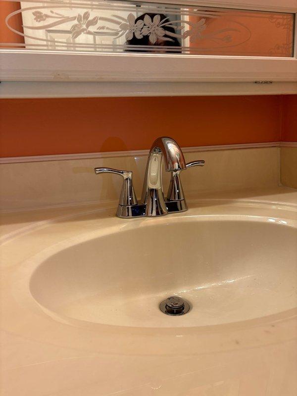 Diagnosed and repaired bathroom faucet leaking into cabinet below. Inspected the plumbing connections inside the wooden cabinet housing the PVC pipe fittings and resolved the leak. Verified proper operation of the chrome dual-handle faucet with no further leakage present.