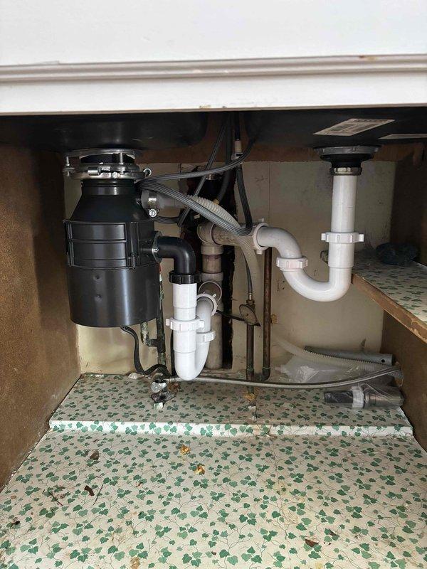 Responded to service call for clogged kitchen sink with standing water in both basins of black composite double-sink. Diagnosed and cleared blockage in the drainage system connected to garbage disposal unit, restoring proper water flow through the P-trap configuration and PVC drain pipes.