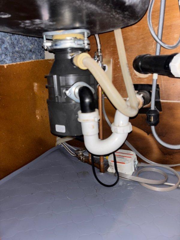 Responded to service call for garbage disposal leak and insufficient hot water production. Inspected under-sink plumbing configuration including black garbage disposal unit connected to PVC drain pipes with P-trap assembly. No active leaks were observed during inspection, and all connections appeared secure with normal working condition confirmed.