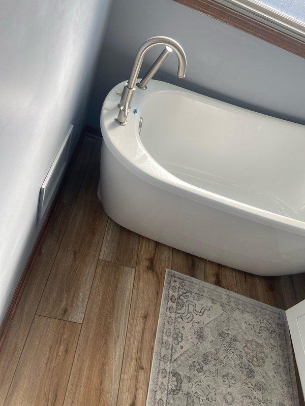 Successfully reinstalled customer's freestanding oval bathtub with brushed nickel fixtures following completion of new wood-look flooring installation. Properly connected water supply lines and drain assembly, then verified proper function with no leaks.