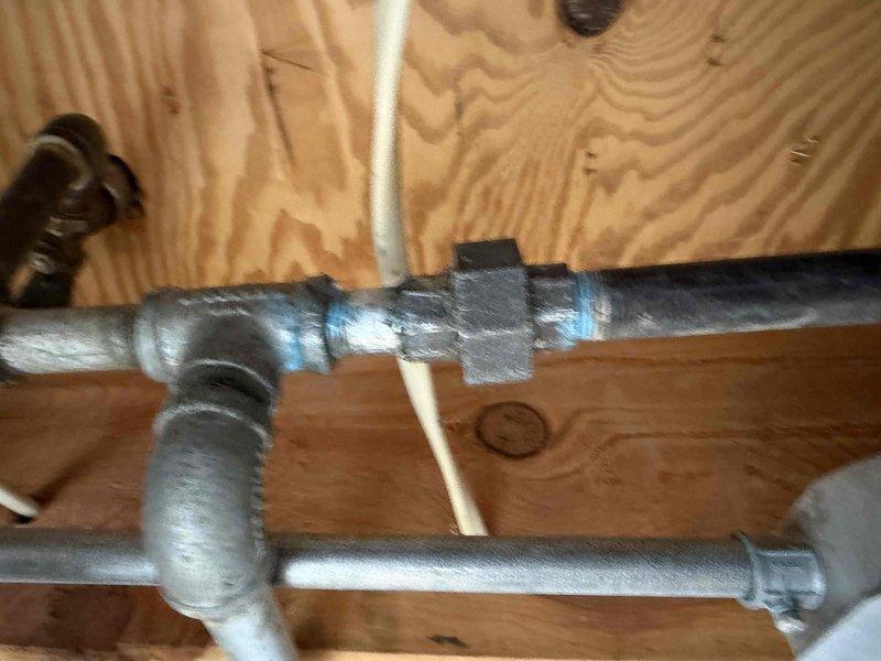 Performed comprehensive gas pressure test on basement gas line system that was previously serviced. Inspection of the galvanized steel piping installation revealed T-junction configurations with potential weak points at union joints. Documentation with photos captured the condition of pipe connections and mounting hardware, including the reddish bracket securing the gas line to wooden joists. No active leak was located during this service visit; system was left operational with recommendations for continued monitoring.