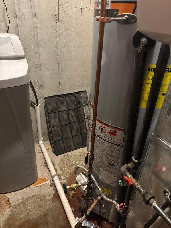 Responded to emergency call for State ProLine tanked water heater experiencing internal failure with significant water leakage from bottom of unit. Upon arrival, confirmed water source had been shut off by customer. Conducted visual inspection and auditory assessment, detecting fountain-like sound indicating internal tank rupture. Inspected basement utility area installation, noting unit was approximately 5-6 years old with copper supply lines, proper venting through galvanized duct, and standard connections. Documented equipment condition through photographs showing water heater alongside existing water softener system. Evaluated extent of damage and determined tank breach required full water heater replacement. Provided customer with repair options and recommendations for new unit installation.