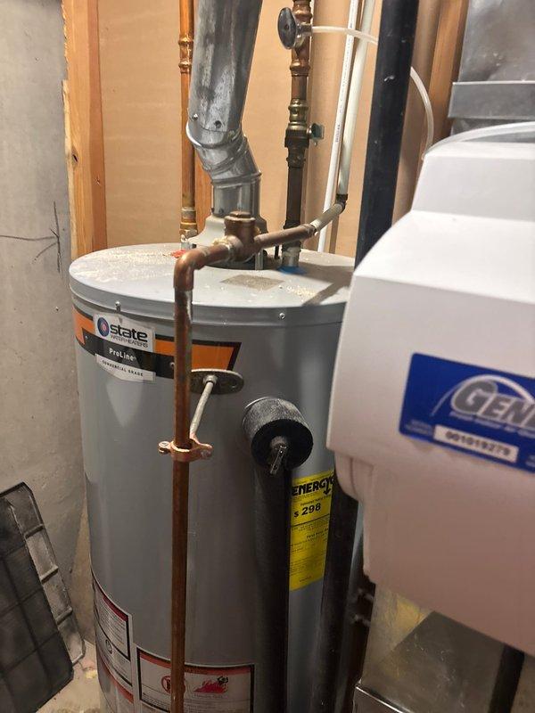 Responded to emergency call for State ProLine tanked water heater experiencing internal failure with significant water leakage from bottom of unit. Upon arrival, confirmed water source had been shut off by customer. Conducted visual inspection and auditory assessment, detecting fountain-like sound indicating internal tank rupture. Inspected basement utility area installation, noting unit was approximately 5-6 years old with copper supply lines, proper venting through galvanized duct, and standard connections. Documented equipment condition through photographs showing water heater alongside existing water softener system. Evaluated extent of damage and determined tank breach required full water heater replacement. Provided customer with repair options and recommendations for new unit installation.