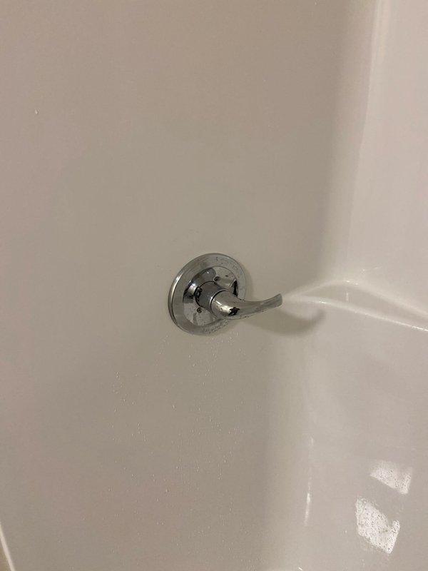 Installed commercial plumbing piping system including PVC supply lines with multiple fittings, elbows, and couplings routed through attic space over insulation. Mounted chrome-finished single-lever shower valve with escutcheon plate on white fiberglass surround, completing bathroom fixture installation.