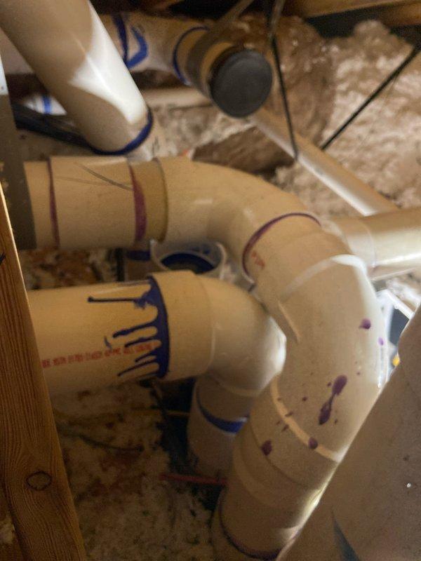 Installed commercial plumbing piping system including PVC supply lines with multiple fittings, elbows, and couplings routed through attic space over insulation. Mounted chrome-finished single-lever shower valve with escutcheon plate on white fiberglass surround, completing bathroom fixture installation.