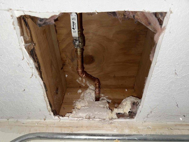 Responded to service call for exterior faucets that were continuously running and failing to shut off properly. Upon arrival, inspected the outside hose bibb assembly with green-handled wheel valve mounted on stone foundation wall. Traced water supply line from exterior valve through wall penetration to access interior plumbing system. Created access opening in interior drywall to expose copper supply piping, wooden framing, and valve connections. Diagnosed faulty valve mechanism preventing proper water shutoff. Repaired/replaced defective components to restore proper operation of exterior faucet control valve. Verified water flow could be fully stopped at valve handle. System tested and confirmed operational with no continued running or leakage.