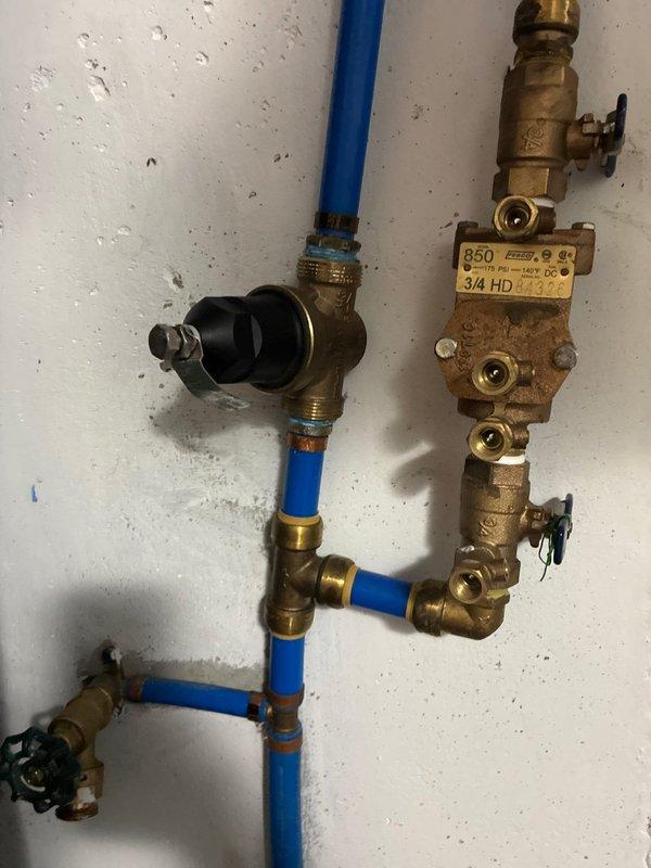 Responded to report of water leaking from tanked water heater in basement. Upon arrival, conducted thorough inspection of the water heater system and associated plumbing components. Identified issues with the water supply system requiring attention to pressure regulation and control valve assembly.

Inspected and verified proper operation of the building's water pressure regulation system, confirming the WATTS pressure gauge reading approximately 100 psi. Examined the complete plumbing manifold assembly including brass fittings, control valves, and pressure regulator mounted on the supply line. Assessed condition of blue CPVC piping connections and multiple brass T-joints, elbow fittings, and shutoff valves with black handles throughout the system.

Addressed the reported leak condition and ensured all connections were secure and functioning properly. Verified proper pressure settings and confirmed all control valves were operational. Documented system configuration including pressure 