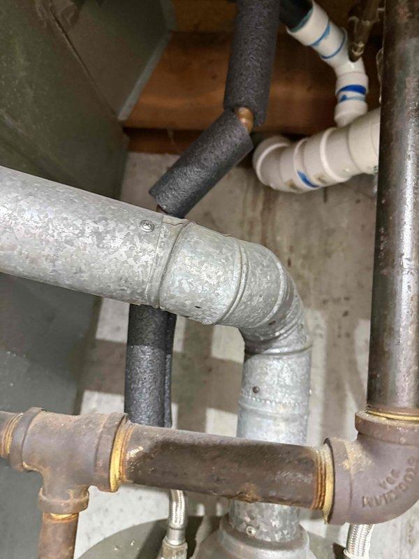 Responded to recall for clogged drain with water backing up from kitchen sink to main bathroom sink. Upon inspection, discovered significant crack in black vertical drain pipe in utility area, which was causing drainage issues and cross-contamination between fixtures. Documented damaged pipe assembly and surrounding plumbing connections including compromised section with irregular opening exposing internal cavity.