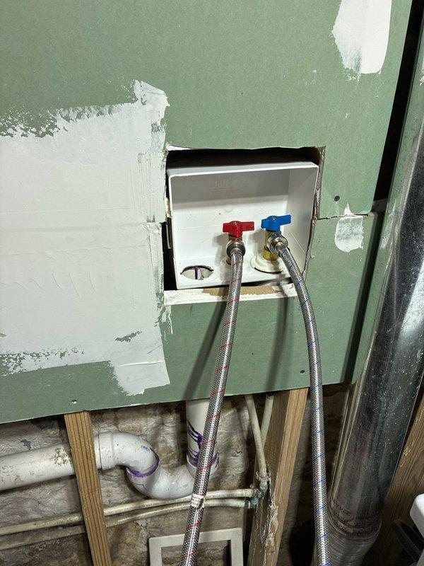 Responded to service call for multiple plumbing concerns including exterior faucet leaking into the house, washing machine supply line leak, and moisture at cast iron to PVC connection on main plumbing stack. Performed comprehensive inspection of all reported areas. Examined exterior hose bibb and traced water intrusion path. Inspected washing machine supply valves with red and blue handles mounted in wall box, noting aged flexible braided supply lines and surrounding PVC drainage system. Assessed main drain stack connection where cast iron transitions to PVC piping, documenting moisture concerns at joint. Photographed all problem areas including pipe connections, shut-off valves, drainage components, and structural conditions for documentation and repair planning. Provided assessment of existing conditions and discussed repair options with homeowner prior to proceeding with any corrective work per customer request.