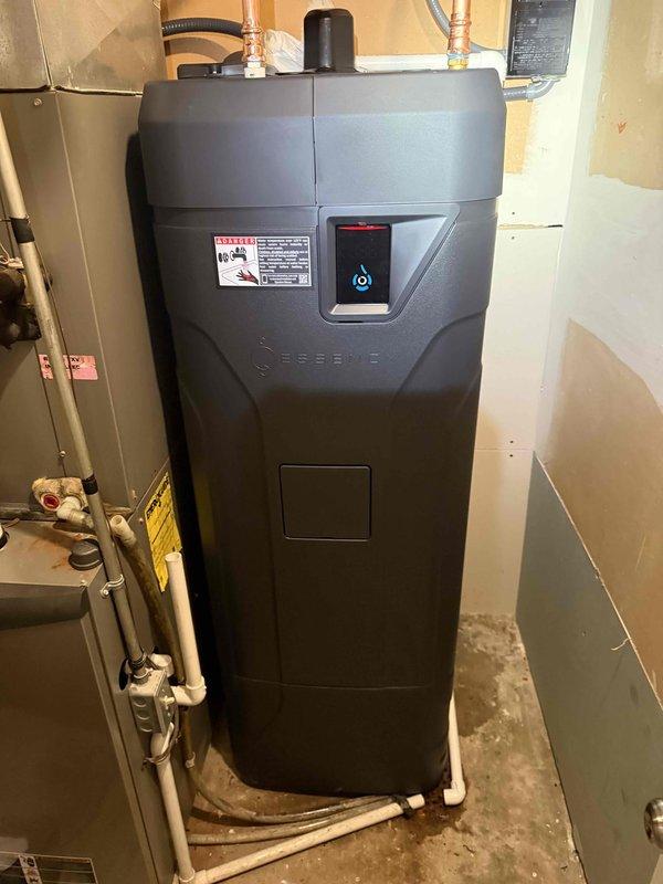 Installed Essency EXR on-demand electric water heater, 50-gallon capacity with 80-gallon equivalent output and 0.93 UEF rating. Connected copper supply lines to unit, established proper drainage with PVC piping, and integrated electrical connections through wall-mounted junction box. Positioned unit in basement utility area adjacent to existing HVAC system with appropriate clearances, verified digital display panel functionality, and confirmed all plumbing connections are secure and leak-free.