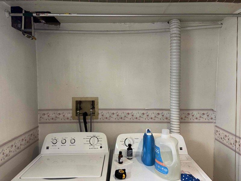 Conducted site assessment for water heater and mechanical equipment relocation in laundry room area. Documented existing plumbing infrastructure including supply lines, drain system with P-trap configuration, and current water heater connections. Evaluated wall cavity access point and existing pipe routing to determine feasibility and requirements for proposed relocation project.