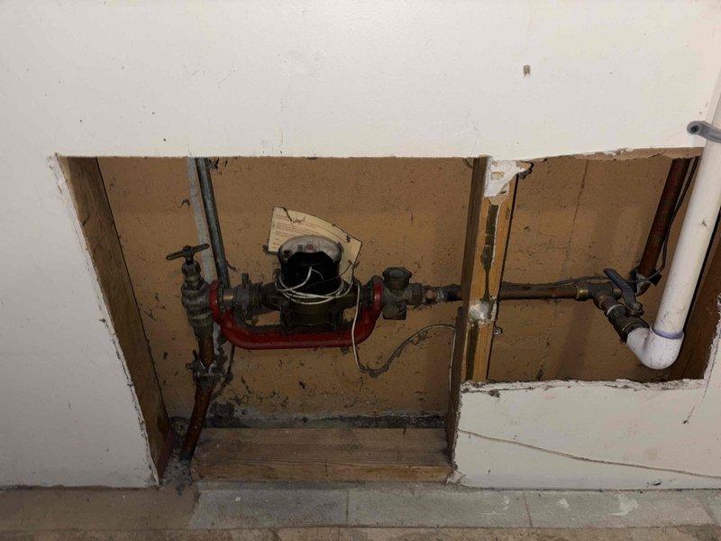 Conducted site assessment for water heater and mechanical equipment relocation in laundry room area. Documented existing plumbing infrastructure including supply lines, drain system with P-trap configuration, and current water heater connections. Evaluated wall cavity access point and existing pipe routing to determine feasibility and requirements for proposed relocation project.