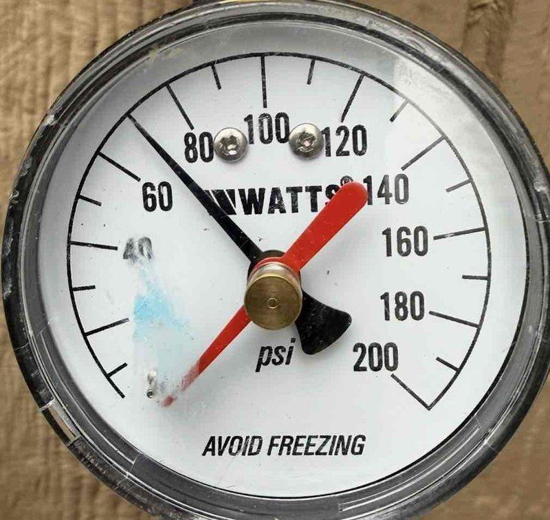 Completed comprehensive whole home plumbing inspection from 8am to 12pm, including tankless water heater flush service. Inspection revealed pink PVC main water line installation in basement utility area with brass shut-off valve assembly showing visible corrosion and weathering on copper fittings requiring monitoring. Documented pressure gauge readings on water system, noting dual-scale gauge displaying measurements in watts and psi with functional black and red indicator needles. All plumbing systems assessed for proper operation, potential leaks, and code compliance throughout the property.