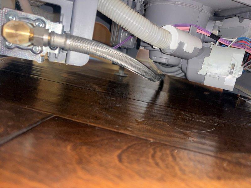 Responded to emergency leak detection call where water supply had been shut off due to active leak from dishwasher penetrating through kitchen floor into basement below. Performed visual inspection of dishwasher water supply connections, including braided stainless steel flex line and brass shut-off valve, as well as drain hose assembly with corrugated white flexible tubing and gray plastic fittings. Examined dishwasher interior chamber, spray arm assembly, and mounting components to identify source of water intrusion causing basement damage.