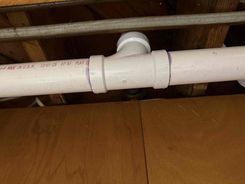 Redirected kitchen drain line in crawl space per approved specifications. Installed new white PVC drainage piping with proper fittings including T-junction connections to accommodate revised drain routing. All joints were properly primed and cemented following plumbing code requirements. New drainage configuration successfully diverts kitchen waste line to meet updated sewer lateral connection point.