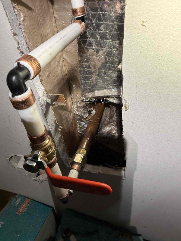 Responded to leak detection request following HVAC contractor observation of water intrusion. Investigated interior plumbing system through wall access point, inspecting PVC supply lines with copper fittings and red-handled shutoff valve for signs of active leaks or moisture damage. Examined exterior hose bib and associated connections, checking valve body, handle assembly, and nearby bundled service lines for potential leak sources. Documented conditions of both interior wall cavity plumbing and exterior spigot installation with photographic evidence to assist in determining leak origin point between indoor pipe system and outdoor faucet assembly.