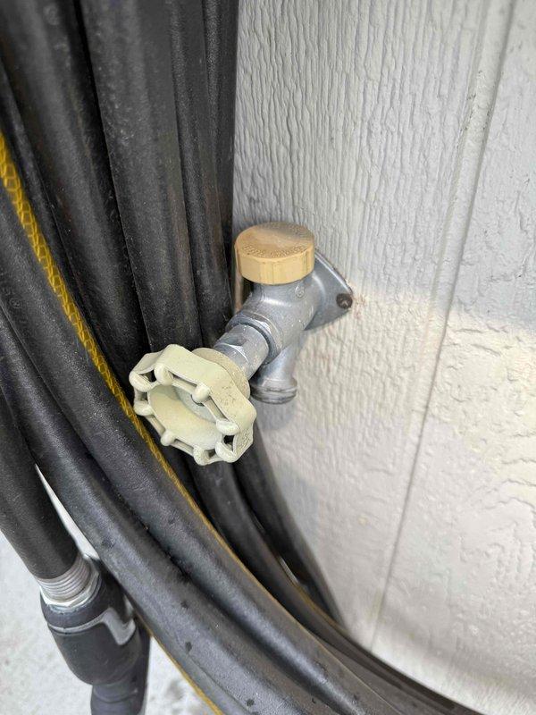 Responded to leak detection request following HVAC contractor observation of water intrusion. Investigated interior plumbing system through wall access point, inspecting PVC supply lines with copper fittings and red-handled shutoff valve for signs of active leaks or moisture damage. Examined exterior hose bib and associated connections, checking valve body, handle assembly, and nearby bundled service lines for potential leak sources. Documented conditions of both interior wall cavity plumbing and exterior spigot installation with photographic evidence to assist in determining leak origin point between indoor pipe system and outdoor faucet assembly.