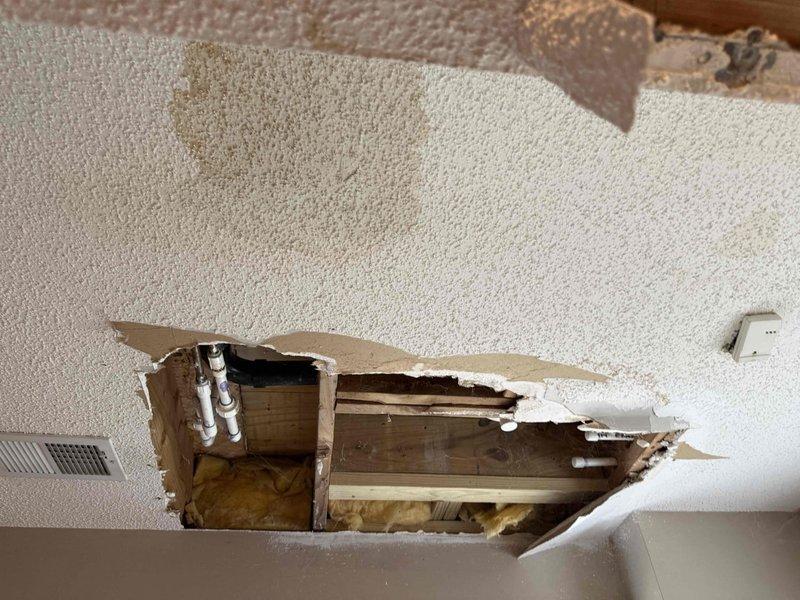 Responded to reported water leak originating from bathroom and causing ceiling collapse in basement below. Upon arrival, performed comprehensive leak location inspection of exposed plumbing system through damaged ceiling cavity. Investigation revealed bathroom plumbing infrastructure including white PVC drain lines and copper supply lines with shutoff valve assembly running through floor joists. Extensive water damage evident with collapsed textured drywall ceiling, exposed fiberglass insulation, and compromised structural framing. Traced leak source through visual inspection of pipe configuration, joints, and valve connections visible in exposed cavity. Documented plumbing system layout including supply and drain line routing for repair recommendations. Customer advised of findings and provided estimate for necessary repairs to address leak source and restore ceiling structure.