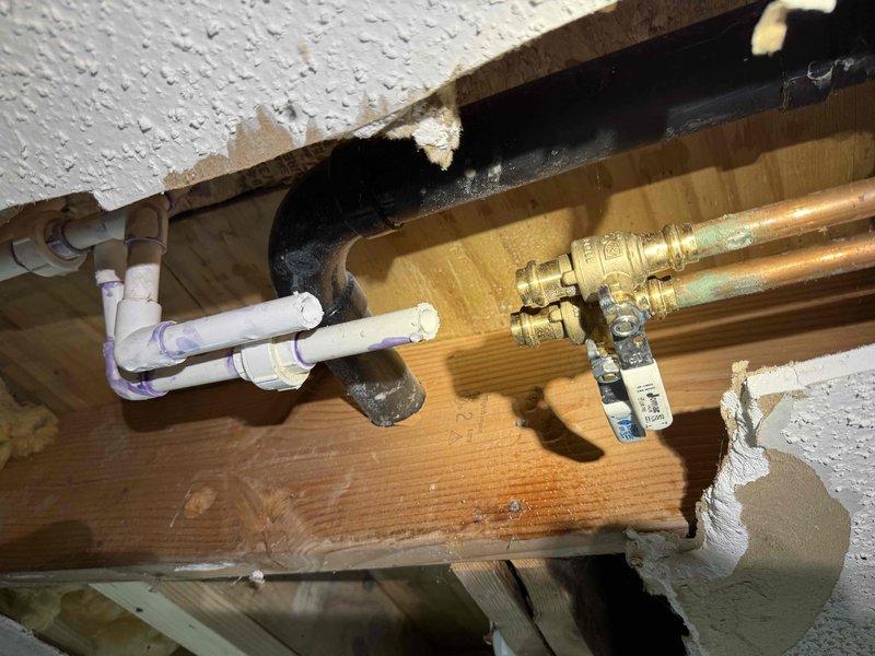 Responded to reported water leak originating from bathroom and causing ceiling collapse in basement below. Upon arrival, performed comprehensive leak location inspection of exposed plumbing system through damaged ceiling cavity. Investigation revealed bathroom plumbing infrastructure including white PVC drain lines and copper supply lines with shutoff valve assembly running through floor joists. Extensive water damage evident with collapsed textured drywall ceiling, exposed fiberglass insulation, and compromised structural framing. Traced leak source through visual inspection of pipe configuration, joints, and valve connections visible in exposed cavity. Documented plumbing system layout including supply and drain line routing for repair recommendations. Customer advised of findings and provided estimate for necessary repairs to address leak source and restore ceiling structure.