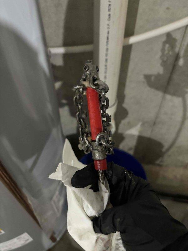 Responded to after-hours call for basement drainage issue where homeowner was uncertain whether sump pump or drain system was malfunctioning. Upon inspection, found existing sump pump with suspended discharge pipe configuration secured by chain mounting system. Observed significant standing water accumulation on basement floor surrounding PVC discharge pipe, with visible water pooling and ripple patterns indicating active drainage problems. Concrete floor exhibited extensive yellow and brown staining consistent with chronic moisture infiltration and mineral deposits from prolonged water exposure. Assessed mechanical components including pump discharge assembly and drainage infrastructure. Documented conditions showing compromised water management system requiring repairs to restore proper functionality and prevent continued basement flooding.