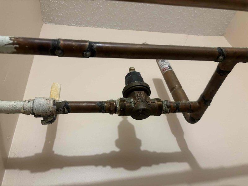 Responded to reported water heater leak at copper pipe fittings in kitchen closet location. Upon inspection, identified aging copper supply lines with significant corrosion and oxidation showing characteristic brown patina consistent with extended service life. The pressure reducing valve assembly and associated threaded connections exhibited wear and deterioration at multiple fitting points, confirming the source of reported water leakage. Documented existing plumbing configuration including corroded copper piping, pressure regulation components, and mounting hardware for service records and recommended repairs.