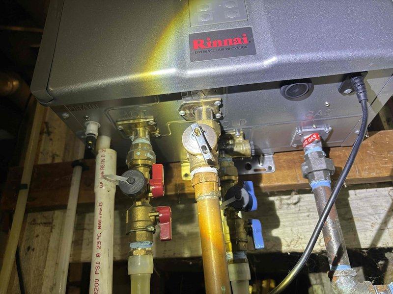 Completed annual plumbing maintenance inspection on Rinnai tankless water heater system. Inspected all service shutoff valves, ball valves, and plumbing connections beneath unit for proper operation and signs of leaks. Verified pressure relief valve functionality, checked brass fittings and compression connections for integrity, and confirmed all hot and cold water supply lines were secure with no visible corrosion or deterioration.