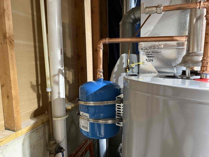 Completed installation of a 40-gallon gas-fired water heater with thermal expansion tank in residential utility space. Configured all copper supply line connections with brass shut-off valves, installed proper venting with metallic duct work and sealed connections, and mounted blue thermal expansion tank to accommodate system pressure fluctuations. All plumbing connections were secured with appropriate fittings and tested for proper operation.