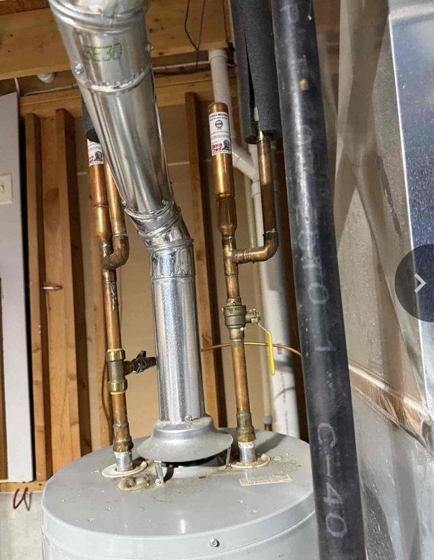 Completed installation of a 40-gallon gas-fired water heater with thermal expansion tank in residential utility space. Configured all copper supply line connections with brass shut-off valves, installed proper venting with metallic duct work and sealed connections, and mounted blue thermal expansion tank to accommodate system pressure fluctuations. All plumbing connections were secured with appropriate fittings and tested for proper operation.
