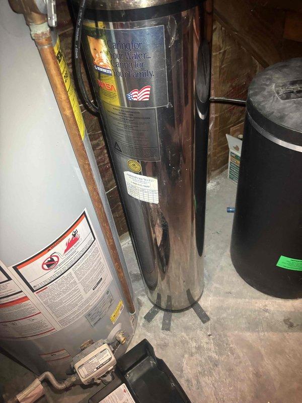 Conducted estimate for servicing Puronics water softener system located in basement utility area. Inspected water treatment equipment including stainless steel brine tank, softener resin tank, and associated plumbing connections with copper supply lines and PVC drainage piping. Assessed system condition, documented current installation configuration, and identified service requirements for proper water softening operation.