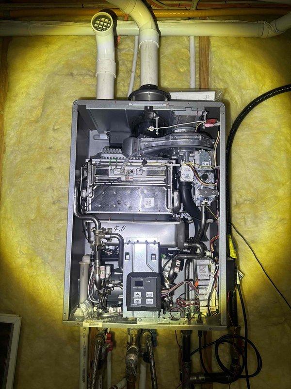 Performed maintenance inspection on tankless water heater unit. Removed front access panel to examine internal components including heat exchanger, burner assembly, control boards, and electrical connections. Verified proper operation of all mechanical systems, checked gas line connections and water line fittings for secure installation, and inspected PVC intake and exhaust venting. Documented equipment condition with photos showing clear liquid sample and internal component configuration. All systems found operational with components properly installed and connected.