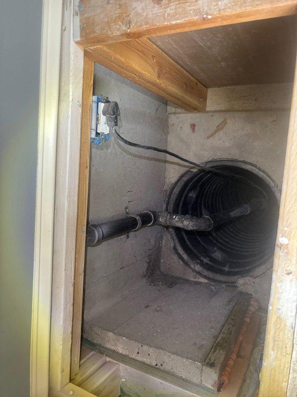 Conducted comprehensive assessment of existing sump pump system in basement utility area to provide replacement estimate. Current sump pump unit operational at time of inspection, housed within enclosed chase space with electrical service and discharge piping in place. Documented existing installation configuration including pump location, electrical connections via wall-mounted outlet box, and drainage routing through corrugated flexible discharge line. Evaluated mechanical chase accessibility, structural framing, and equipment clearances to determine optimal replacement specifications and installation requirements for new sump pump system.