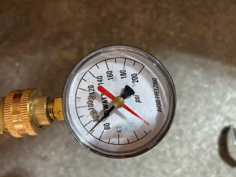 Completed routine plumbing maintenance inspection of one unit. Verified backflow preventer pressure gauge reading at approximately 140 psi within normal operating parameters. Inspected toilet tank internal components including flush valve assembly with red rubber flapper seal and fill valve mechanism with refill tube connection, confirming all components properly installed and functional.