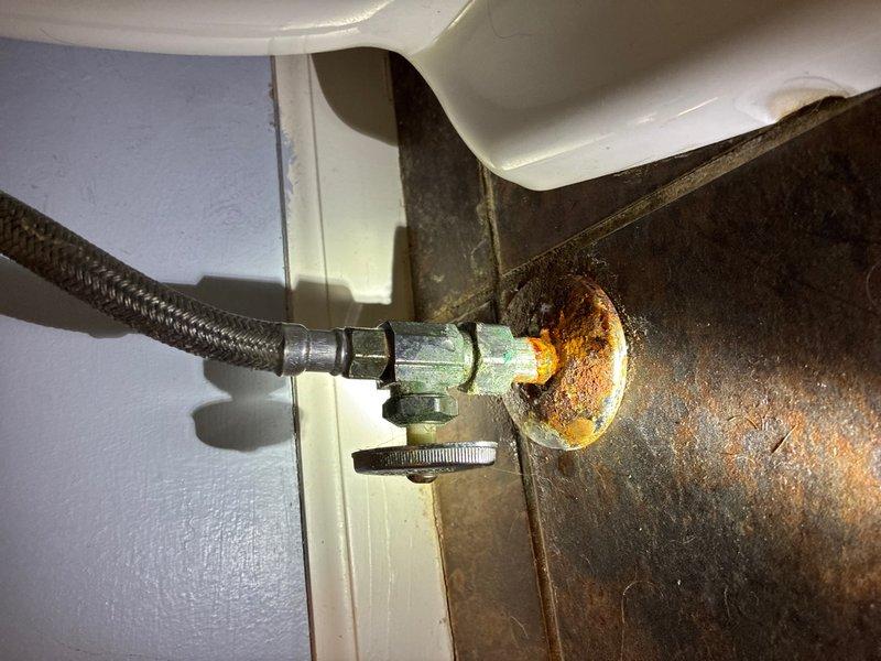 Responded to water leak investigation request due to water staining visible on interior ceiling. Conducted thorough inspection of plumbing fixtures and connections in bathroom area above the affected ceiling. Located source of moisture intrusion at toilet water supply connection point, where extensive corrosion and rust were present on the wall-mounted shut-off valve and surrounding metal escutcheon plate. The braided flexible supply line connection showed significant oxidation and rust halo pattern radiating from the connection point, indicating chronic moisture exposure and potential seepage at the threaded fitting. Documented conditions with photographic evidence showing corroded valve assembly and deteriorated connection components. The rust pattern and moisture damage suggest prolonged intermittent leaking at this fixture supply connection, which would account for the water staining reported on the ceiling below.
