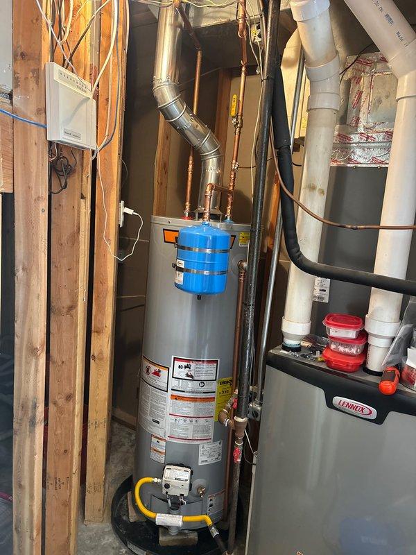 Installed 50-gallon gas water heater with thermal expansion tank mounted at top of unit. Replaced and installed 3/4-inch pressure reducing valve and repaired approximately 3 feet of water supply line. Connected yellow flexible gas line to unit base with shutoff valve, ran copper piping with brass fittings for hot and cold water connections, and installed white PVC drain line at floor level. All plumbing connections secured and tested for proper operation and pressure regulation.