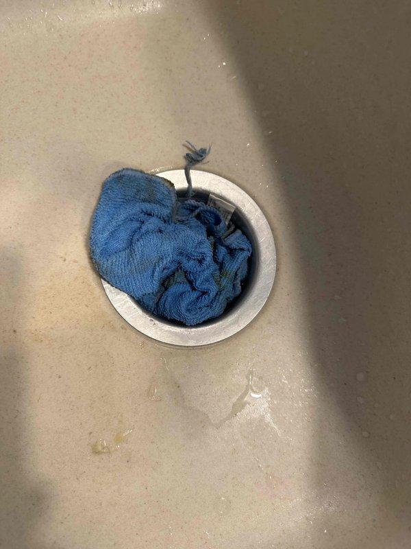 Responded to kitchen sink drainage issue caused by towel lodged in garbage disposal unit. Successfully removed blue terry cloth towel that had become wedged in the disposal mechanism, extracted disposal grinding assembly to clear obstruction, cleaned accumulated debris from impeller blades and grinding chamber, reassembled unit, and tested for proper operation. Disposal now functioning normally with clear drainage restored.