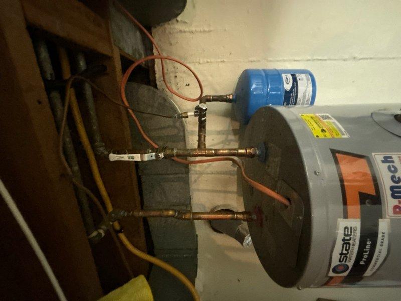Responded to service call for non-operational water heater in basement. Upon inspection, diagnosed State brand tanked water heater with associated plumbing configuration including copper piping, expansion tank, and gas supply line. Evaluated system components including the blue expansion tank mounted horizontally on the piping assembly and verified proper connections throughout the water heater installation. Documented existing equipment setup and provided assessment of necessary repairs to restore hot water functionality.