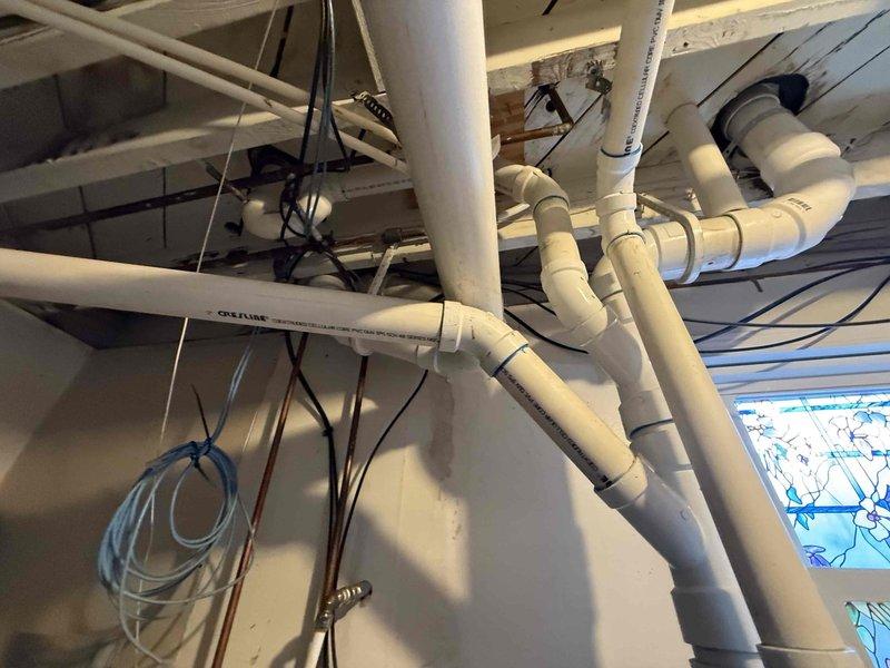 Completed recurring plumbing maintenance inspection of residential water treatment system and overhead drainage infrastructure. Inspected water softener unit for proper operation, verified digital display functionality, and examined copper supply lines and electrical connections for any signs of wear or leakage. Conducted visual assessment of exposed PVC drainage piping system in ceiling area, confirming all pipe connections, joints, and fittings remain secure with no visible deterioration or damage.
