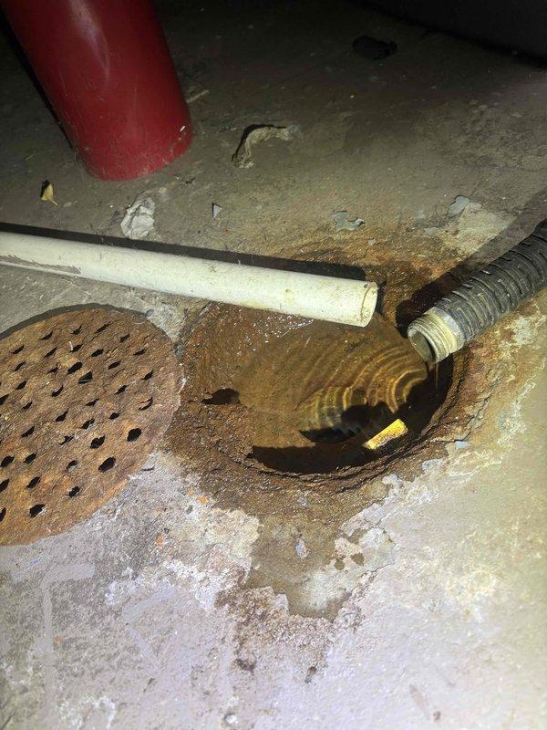 Responded to service call for non-operational sump pump system in residential basement. Upon inspection, found sump pump basin with standing water and malfunctioning pump mechanism. Assessed float switch assembly and pump components for proper operation. Identified issues with pump activation and drainage system performance. Inspected associated discharge piping including PVC outlet lines and corrugated drainage hose connections. Noted significant corrosion on secondary floor drain cover and water staining patterns on basement floor indicating previous drainage concerns. Evaluated sump pit liner, basin depth, and pump positioning. Restored sump pump to full working order, verified float switch operation, and tested pump cycle to ensure proper water evacuation from basin. Confirmed discharge lines were clear and functioning correctly upon completion.