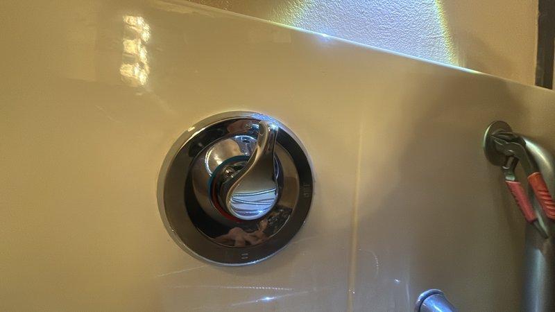 Responded to hallway shower valve malfunction where handle would not turn off water flow. Upon arrival, main water supply had already been shut off by occupant. Removed existing MOEN brand shower valve trim and cartridge assembly from white tiled shower wall. Installed replacement MOEN valve cartridge and reassembled chrome-finished circular control fixture. Tested operation to verify proper function and complete water shutoff capability. Restored main water supply and confirmed no leaks at valve assembly.