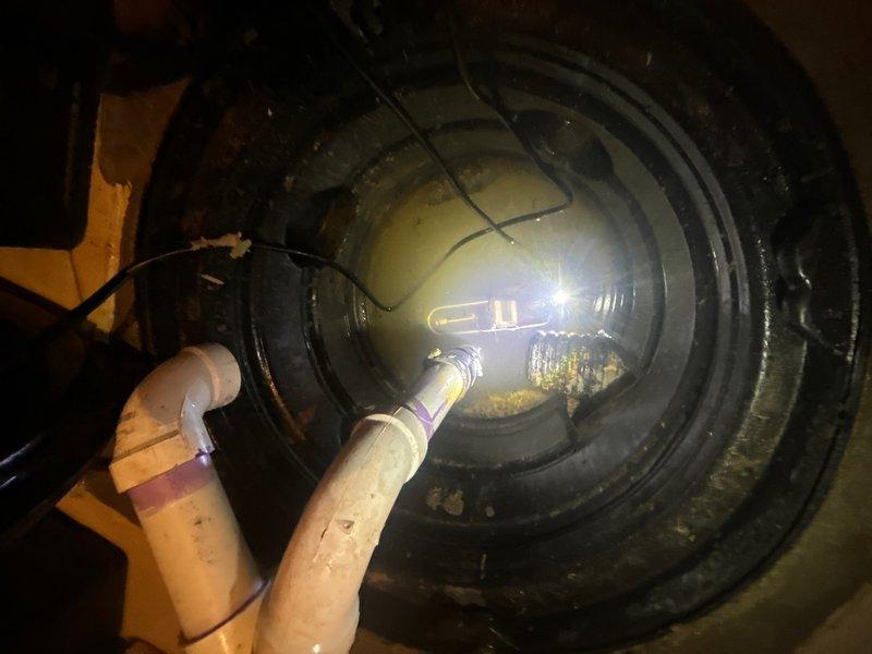 Responded to service call for sump pump malfunction in basement southeast corner of 29-year-old residence. Upon inspection, found significant sediment and debris accumulation at bottom of sump basin, with yellowish-brown material buildup affecting pump operation. Unit was approximately 1–1.5 years old and installed in cylindrical basin with dual PVC discharge lines. Removed accumulated sediment and debris from basin floor that was restricting float switch movement and potentially impacting pump performance. Inspected electrical connections, float switch assembly, and discharge piping configuration. Verified proper operation of pump motor and check valve function. Cleaned basin interior walls showing mineral deposits and staining. Tested pump cycle through multiple activations to ensure proper float engagement and discharge flow. Confirmed adequate drainage through both discharge lines and verified no blockages in piping system. System restored to full operational status.
