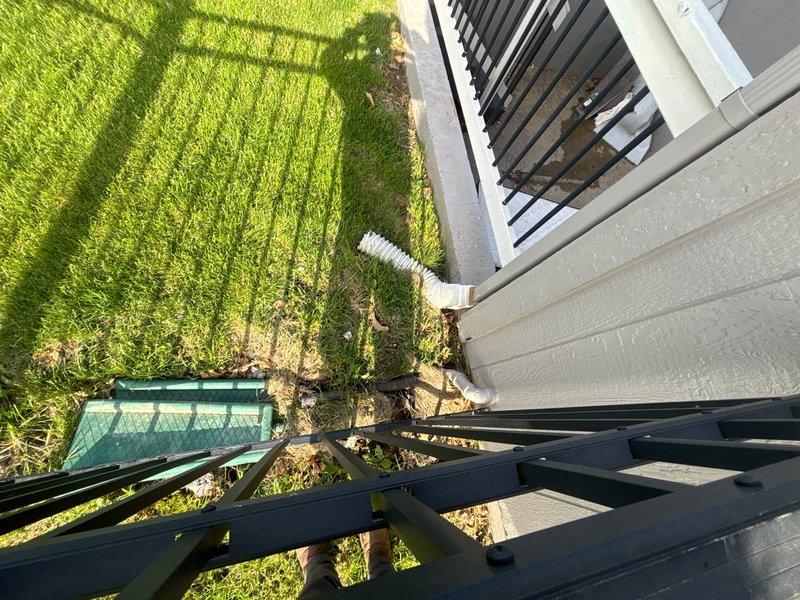 Responded to basement water management concern at residential property. Upon arrival, inspected existing sump pump system and evaluated basement conditions. Found sump pump basin positioned on plywood subflooring near concrete slab transition area. Verified pump operation and assessed discharge line routing from basement to exterior. Confirmed discharge pipe properly directed away from foundation, with white corrugated flexible piping extending from building exterior across lawn area to appropriate drainage point. Examined basement floor conditions, noting moisture patterns on concrete surface and water staining on plywood subflooring surrounding pump location. Tested pump functionality and verified electrical connections secure. System found operational with proper drainage flow established to exterior.